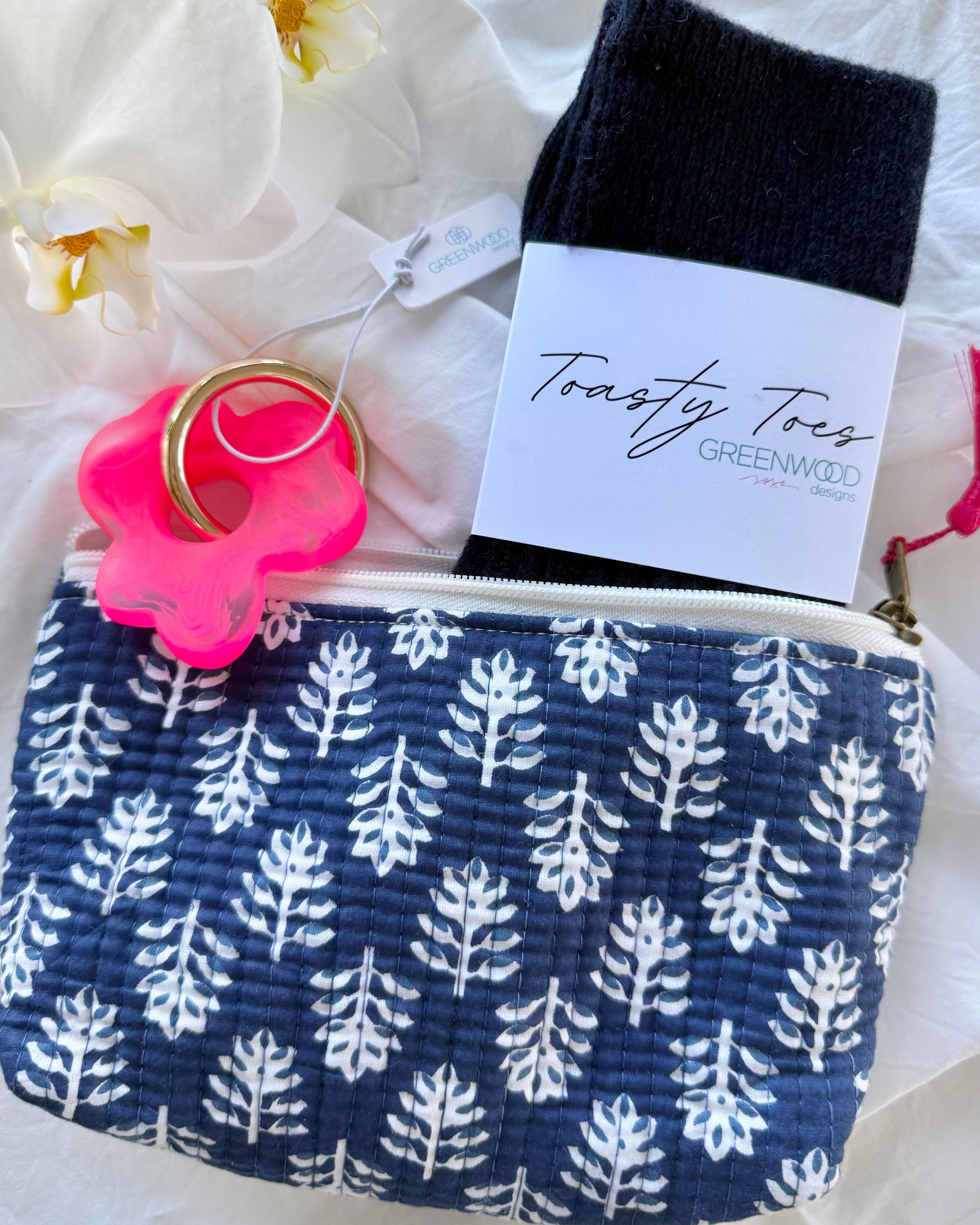Navy pouch with white leaf pattern, black socks, pink item, and white flowers in the background
