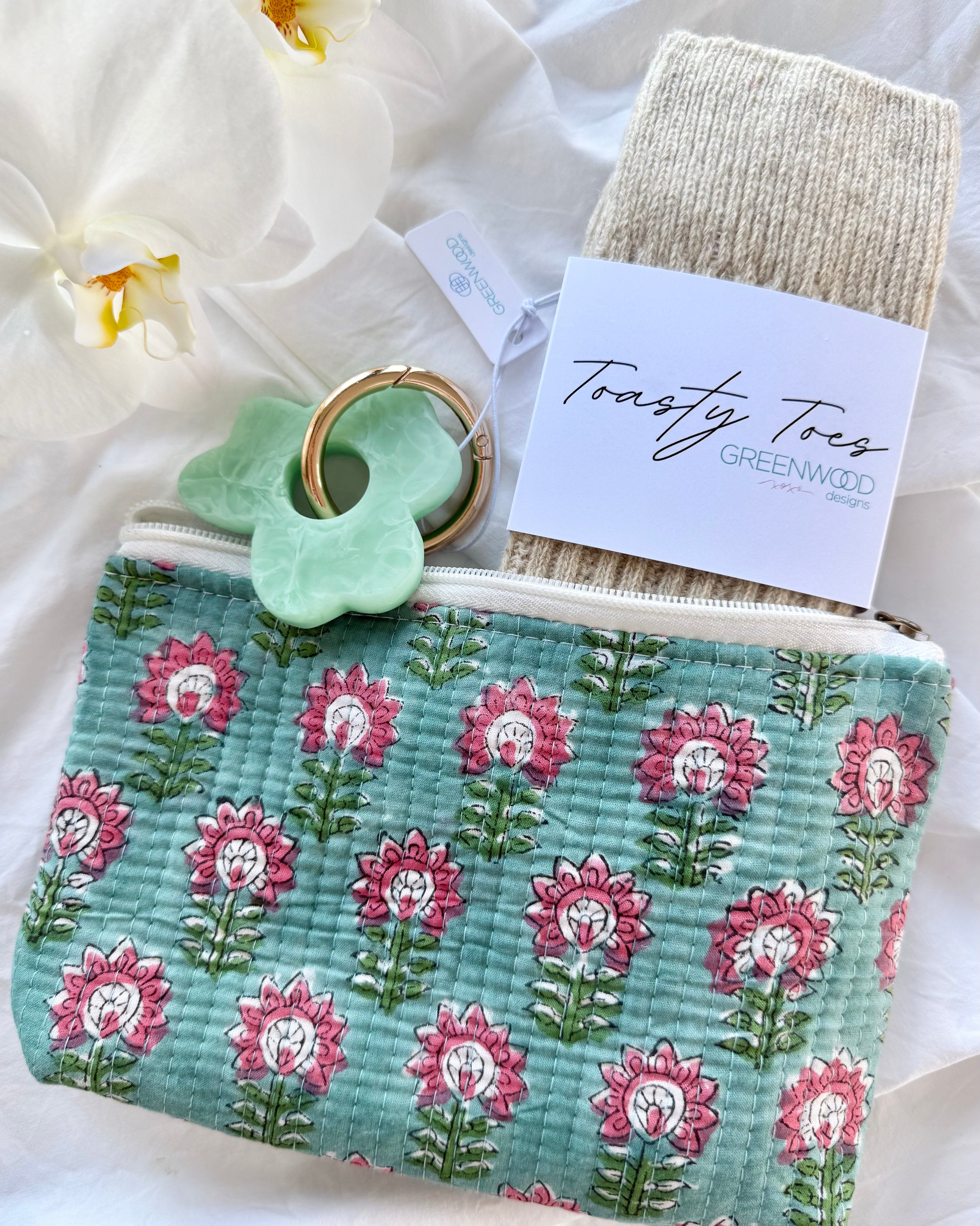 Floral-patterned pouch with a green ring and Toasty Toes branded socks on a white background