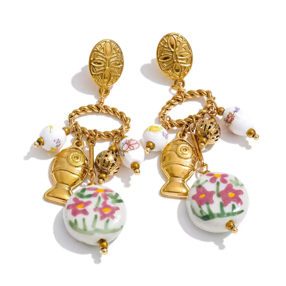 Gold oval stud earrings with a twisted gold hoop holding a gold fish charm, a filigree bead and white ceramic beads painted with pink flowers