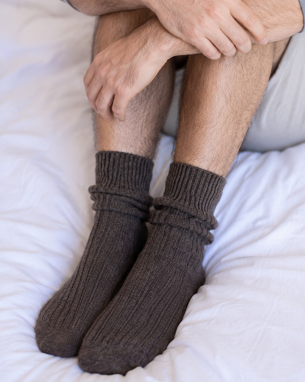 Person wearing brown socks sitting on a white surface