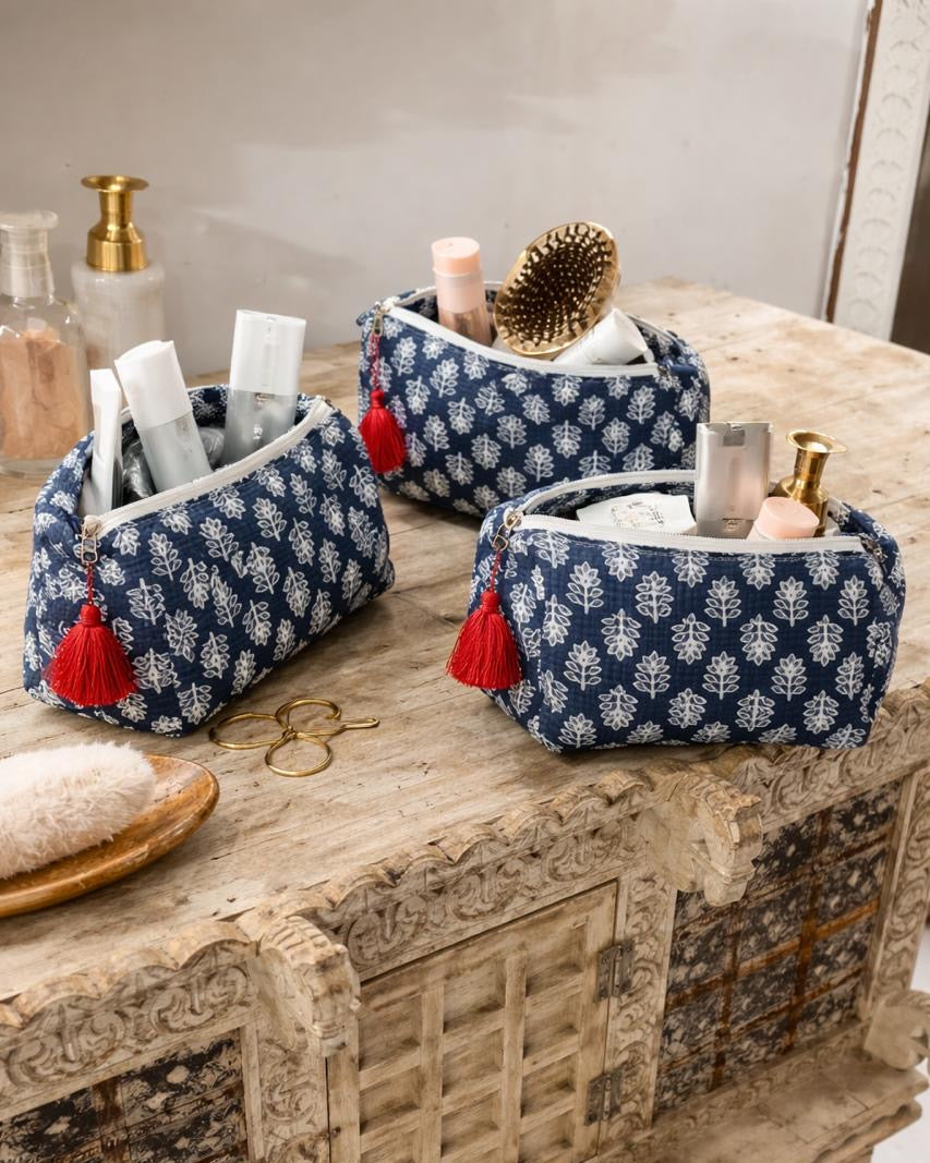 Three blue patterned cosmetic bags with red tassels on a wooden surface.