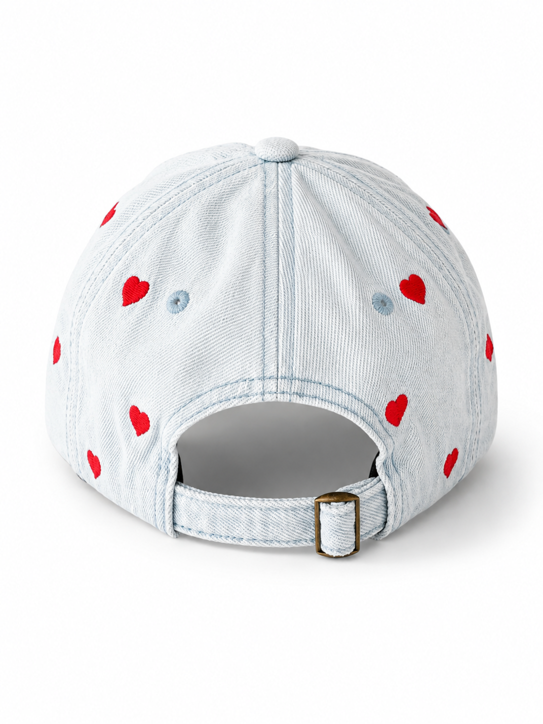 Back view of the light-wash heart-embroidered cap, showing the curved crown and the adjustable strap clipped into its brass buckle.
