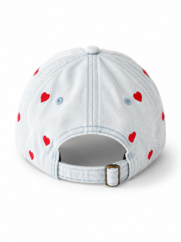 Back view of the light-wash heart-embroidered cap, showing the curved crown and the adjustable strap clipped into its brass buckle.