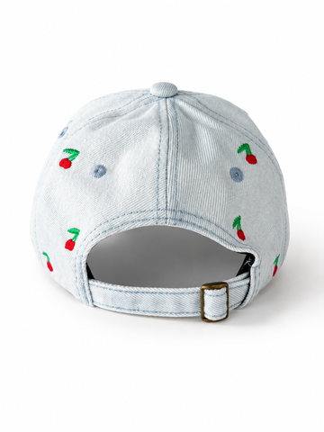 Back view of the light-wash cherry-embroidered cap, showing the curved crown and the adjustable strap clipped into its brass buckle.