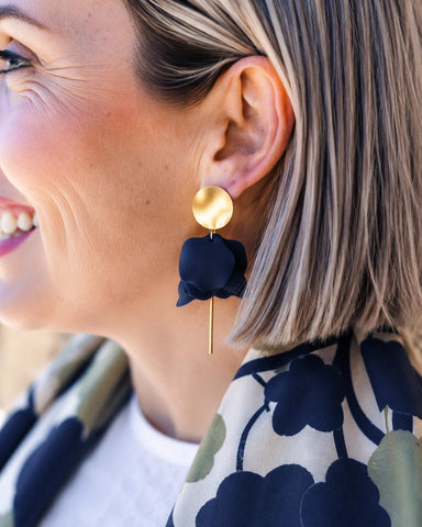 Close-up of a woman wearing gold earrings with blue floral attachments.