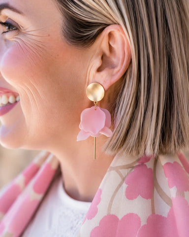 Close-up of a woman wearing pink floral earrings with a blurred background