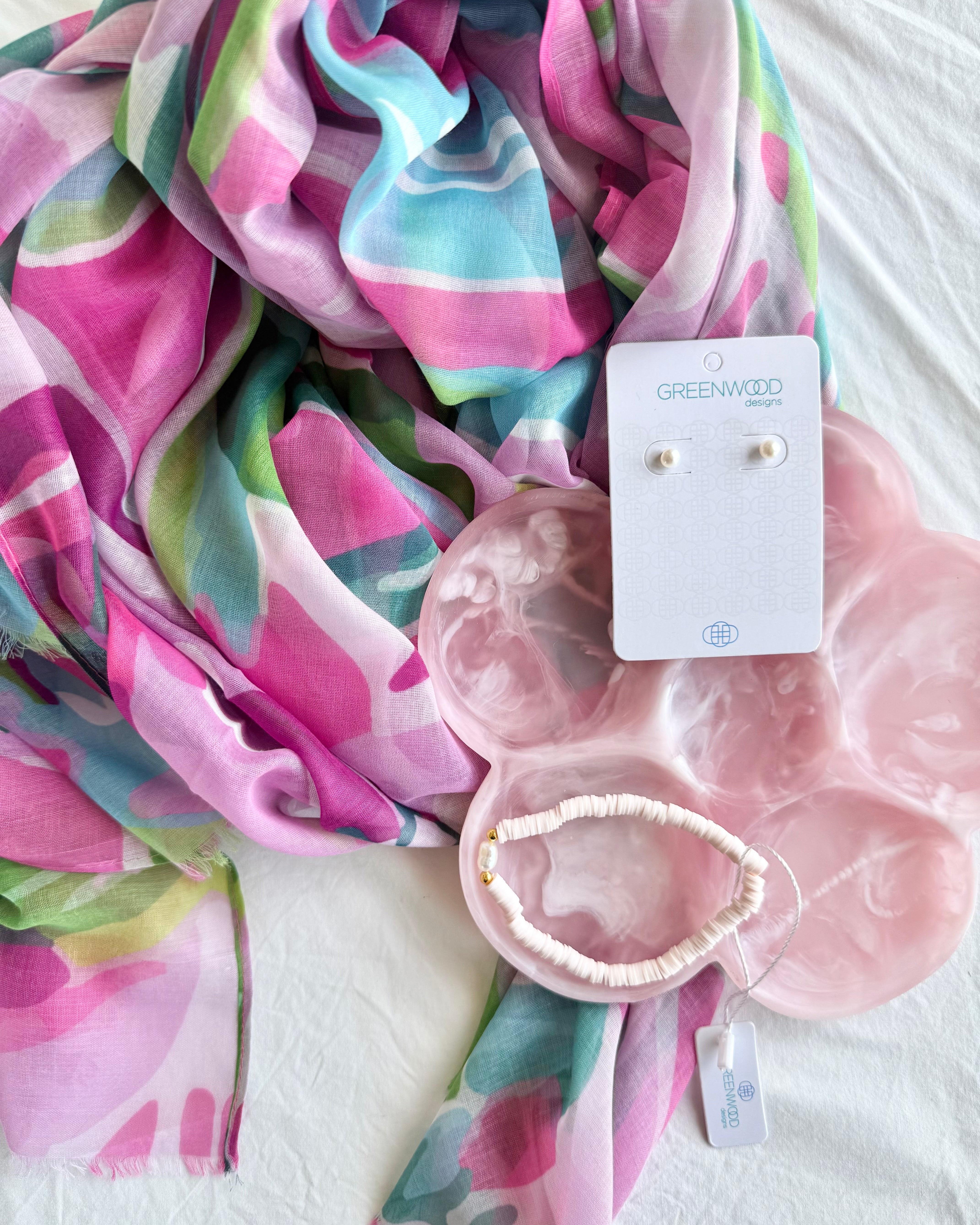 Colorful scarf with pink earrings and a pink pouch on a white surface