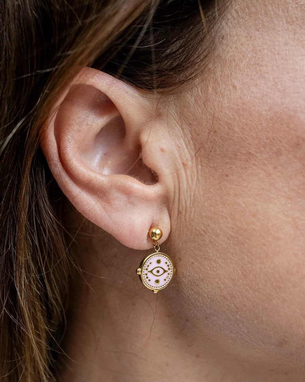 Gold stud earrings with a baby pink enamel evil eye charm dangle