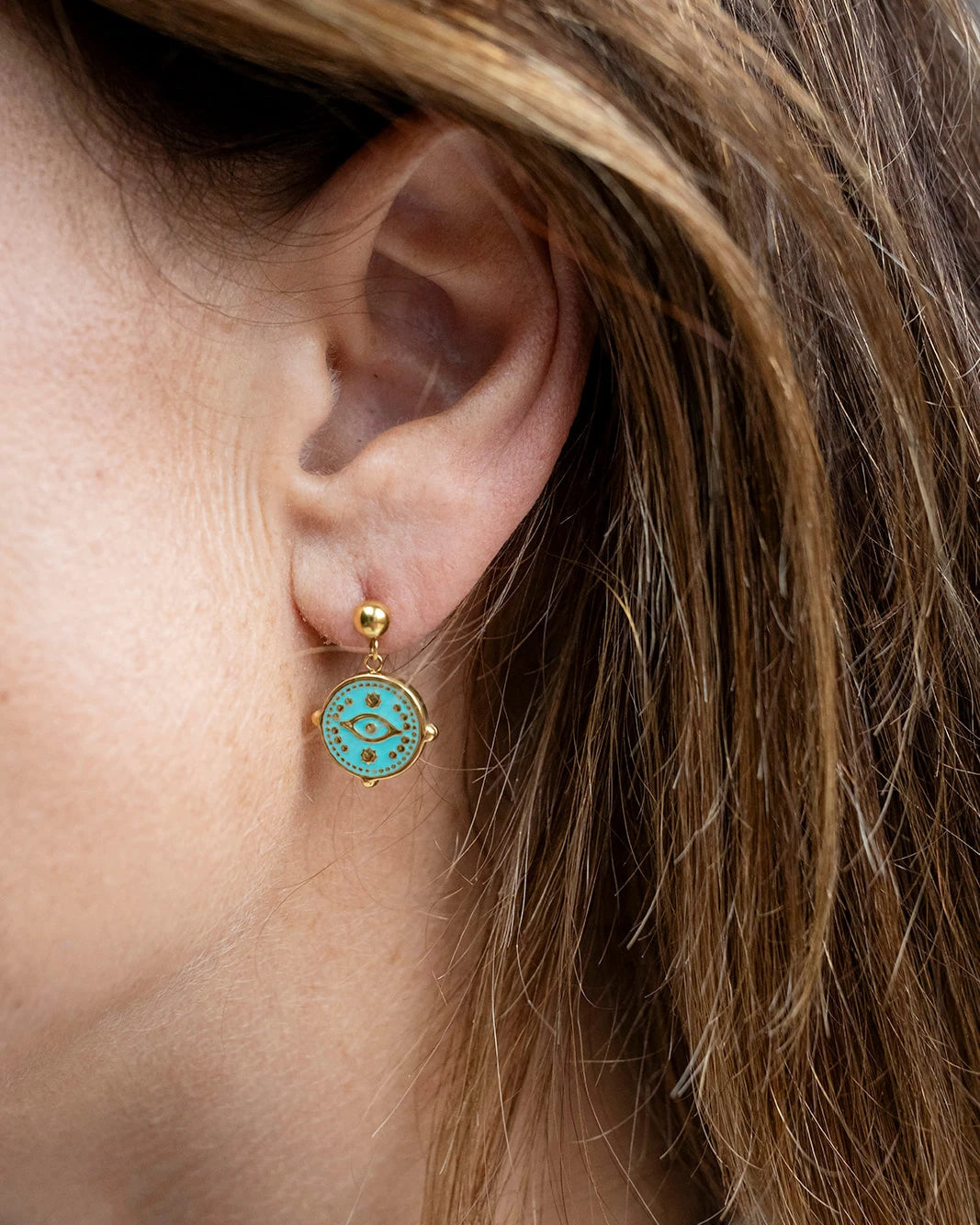 Gold stud earrings with an aqua enamel evil eye charm dangle