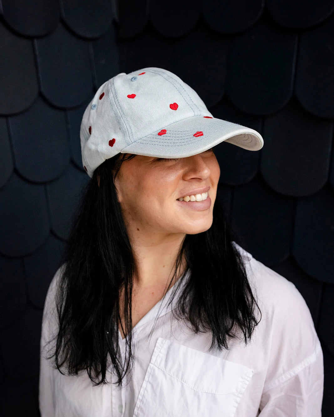 Light-wash denim baseball cap embroidered with small red hearts, front view on a white background.