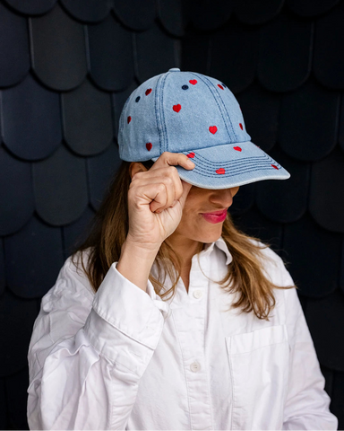 Mid-wash denim baseball cap embroidered with small red hearts, front view on a white background.