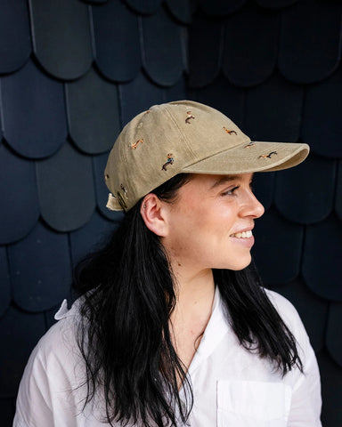 Beige denim baseball cap embroidered with colourful dachshund dogs, front view on a white background.