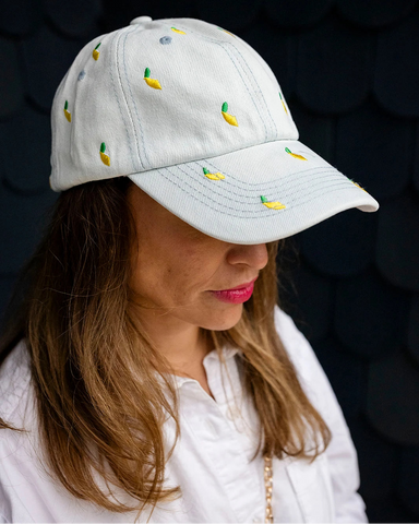 Light-wash denim baseball cap embroidered with small yellow lemons, front view on a white background.