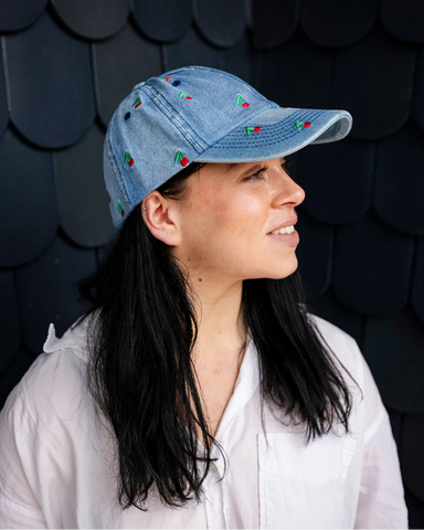 Mid-wash denim baseball cap embroidered with small red cherries, front view on a white background.