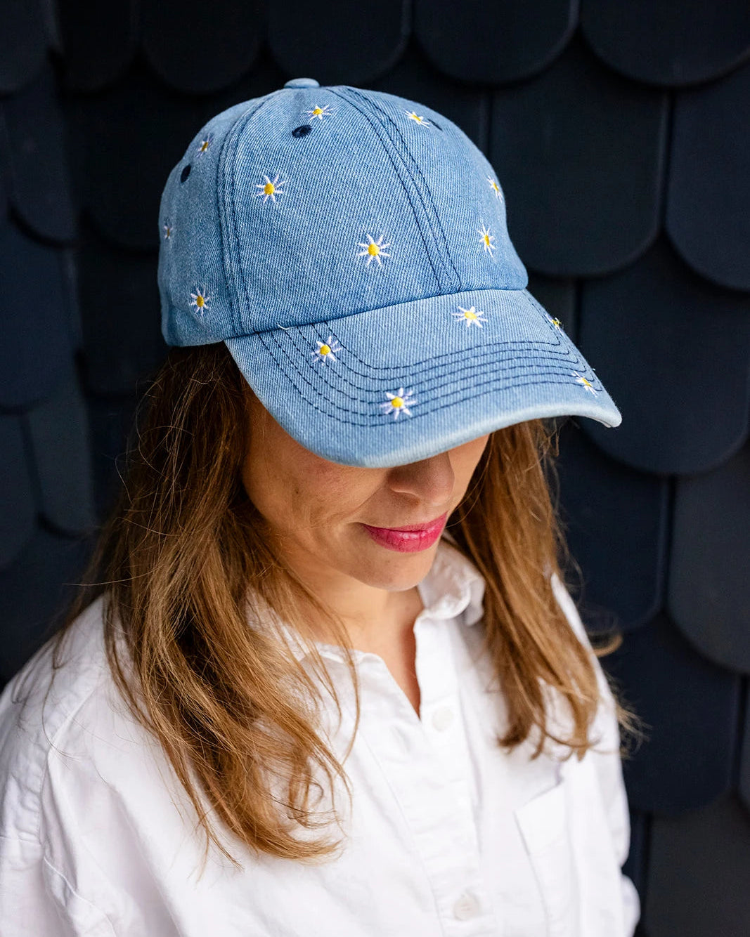 Mid-wash denim baseball cap embroidered with white and yellow daisies, front view on a white background.