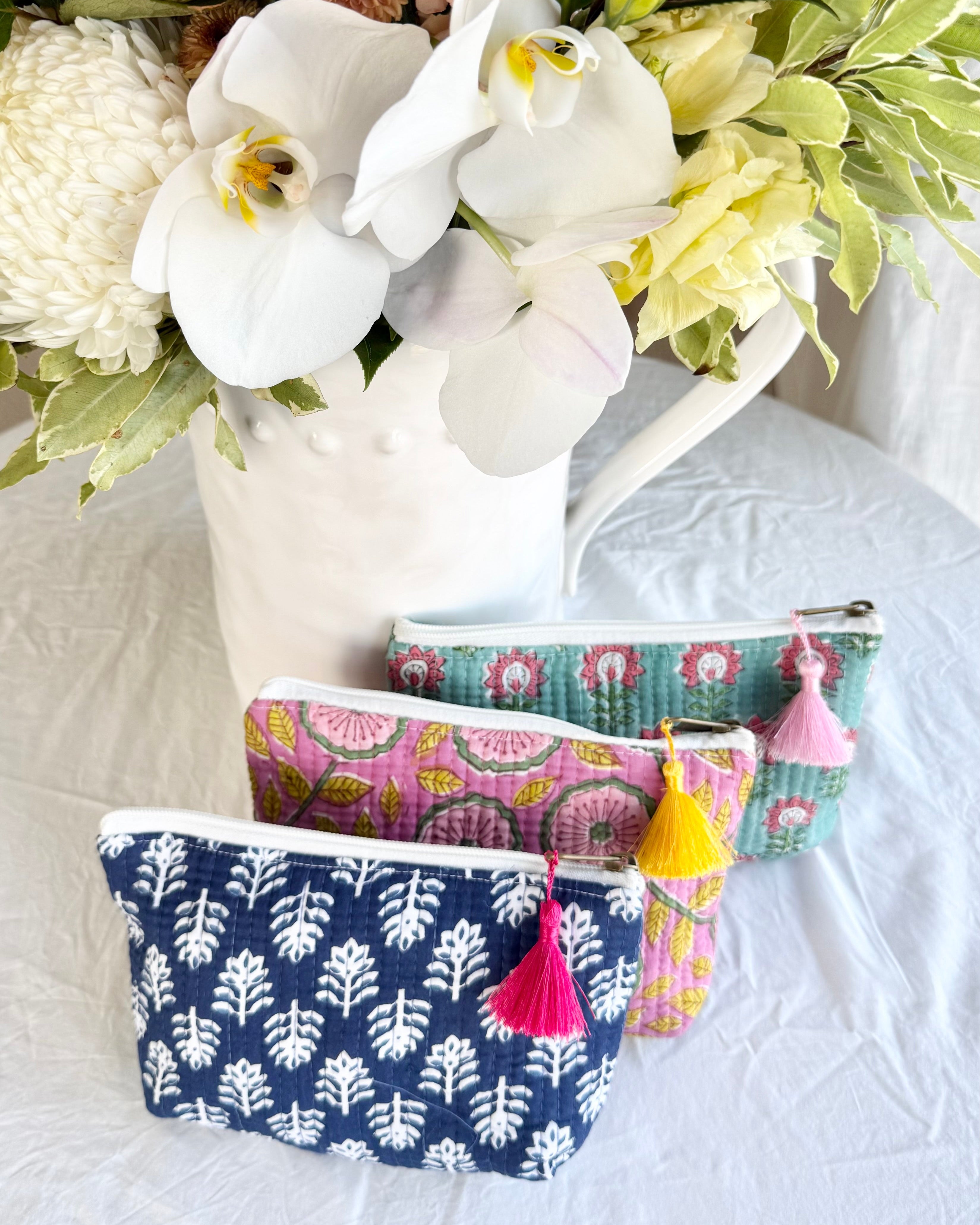 Three patterned pouches with tassels on a white surface with flowers in the background