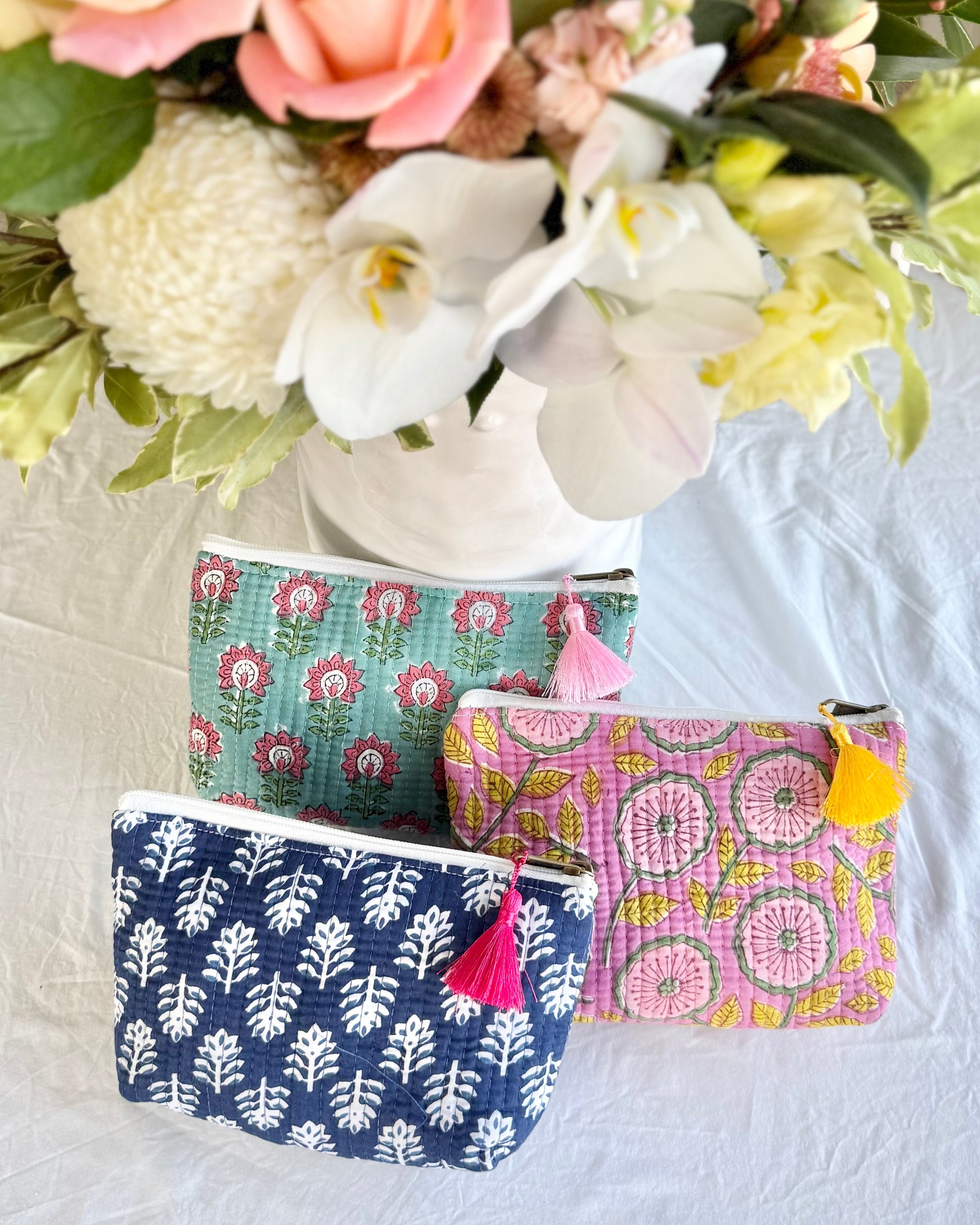 Three patterned pouches with tassels on a white surface with flowers in the background