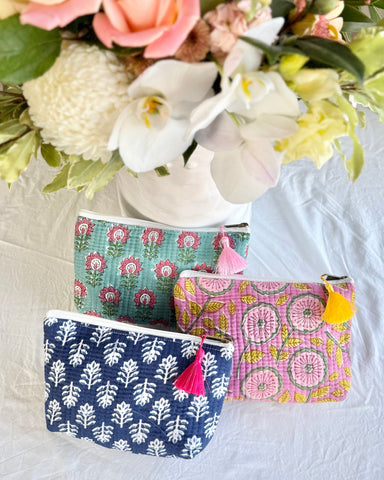 Three patterned pouches with tassels on a white surface with flowers in the background