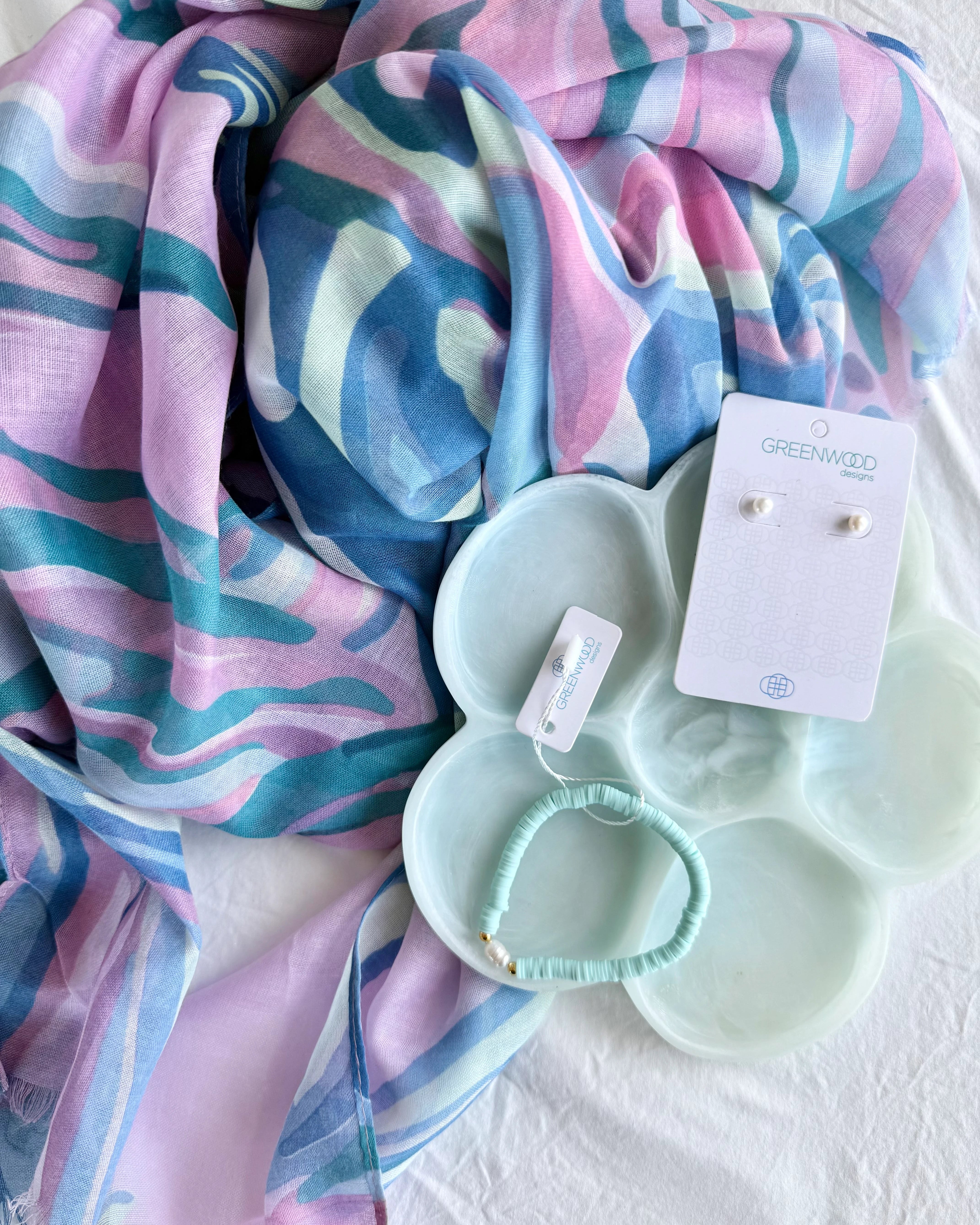 Colorful scarf with a white dish containing a bracelet and earrings on a white background
