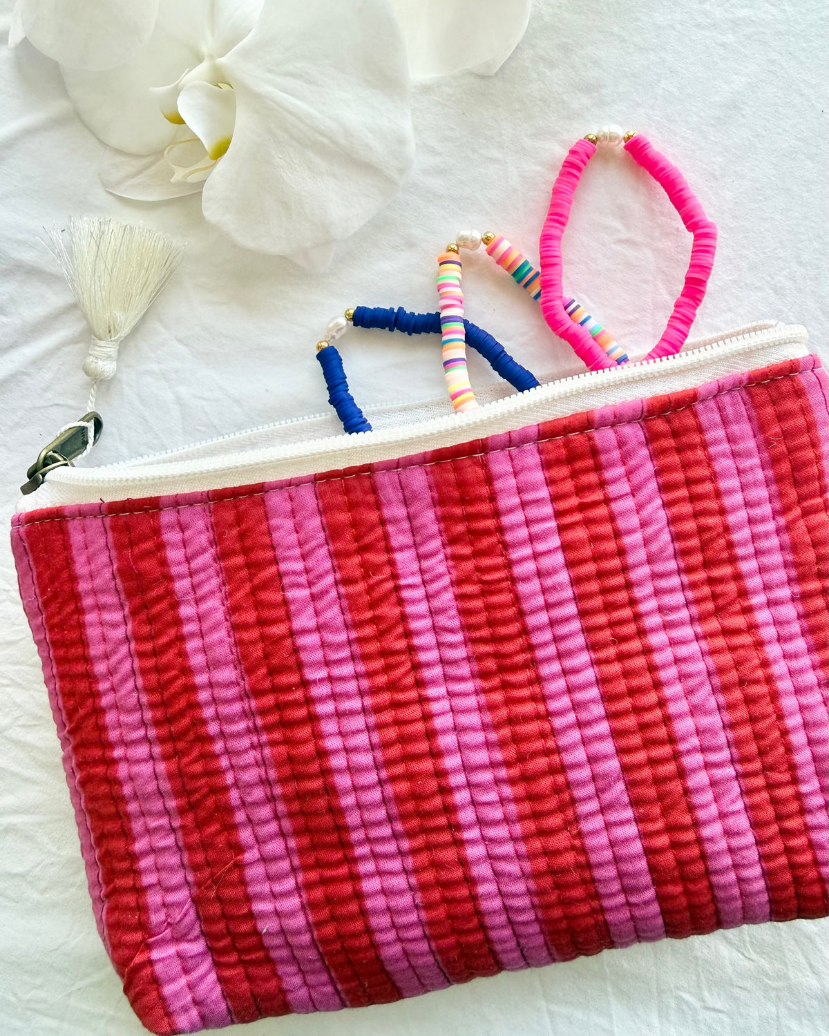 Pink and red striped pouch with colorful hair ties on a white surface