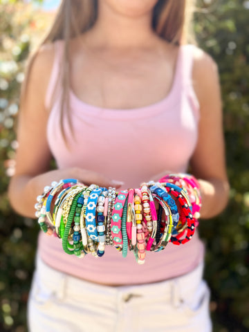 Person holding a collection of colorful bracelets against a blurred natural background