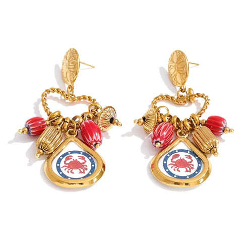 Gold stud earrings with a twisted gold chain loop holding red striped beads, ribbed gold beads and a gold-framed pendant with a red crab on a navy border