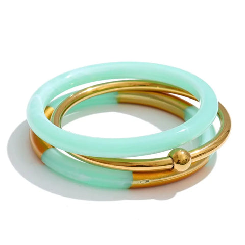 Stack of three bangles: an aqua resin bangle, a polished gold bangle with a gold ball, and a half aqua resin, half gold bangle