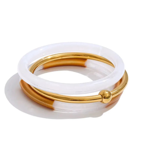 Stack of three bangles: a frosted white resin bangle, a polished gold bangle with a gold ball, and a half white resin, half gold bangle