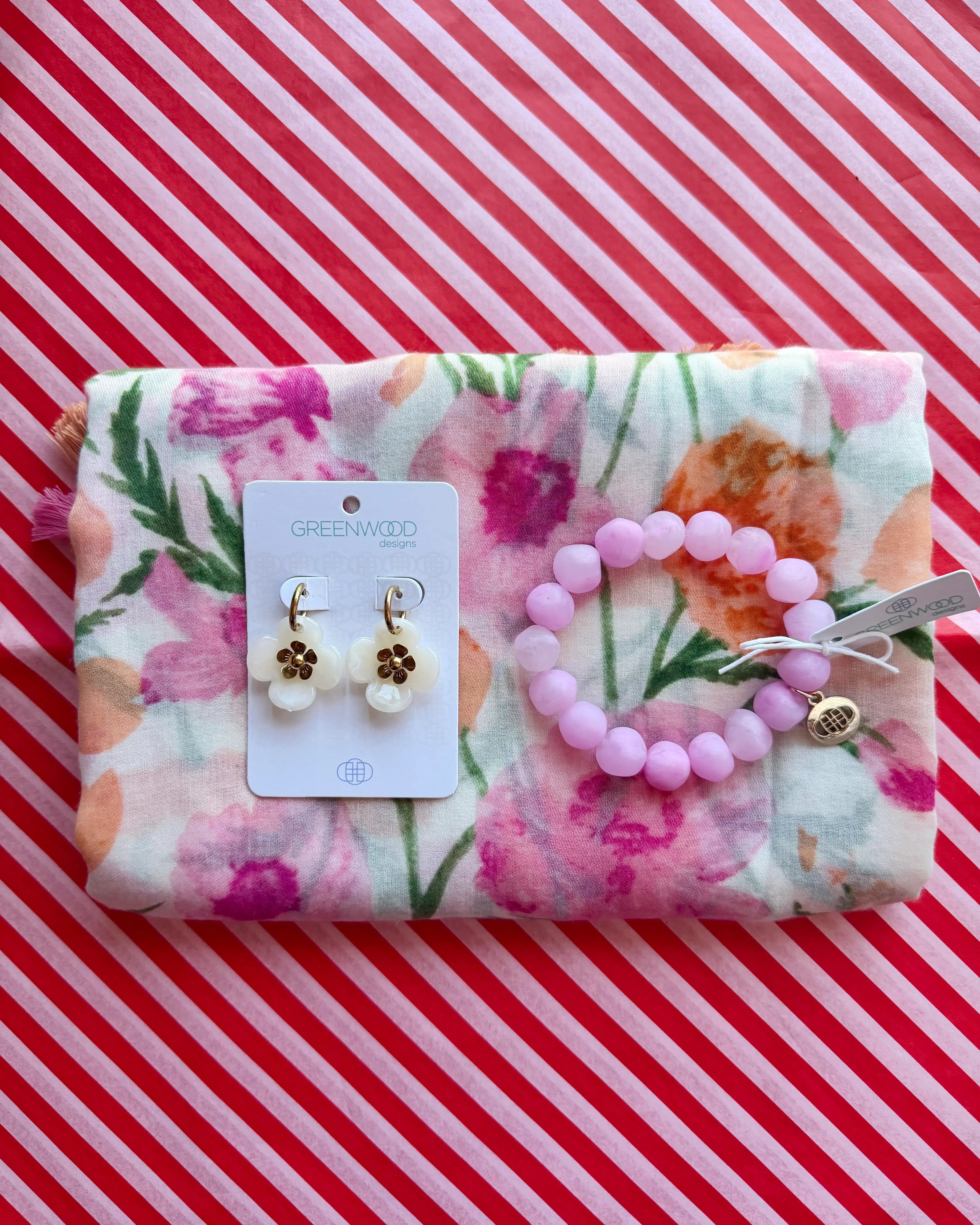 Flat lay of the Coral scarf, white with a coral and pink watercolour floral print, the Light Pink Marble rock bracelet and Willa earrings in Cream on a Greenwood Designs card.