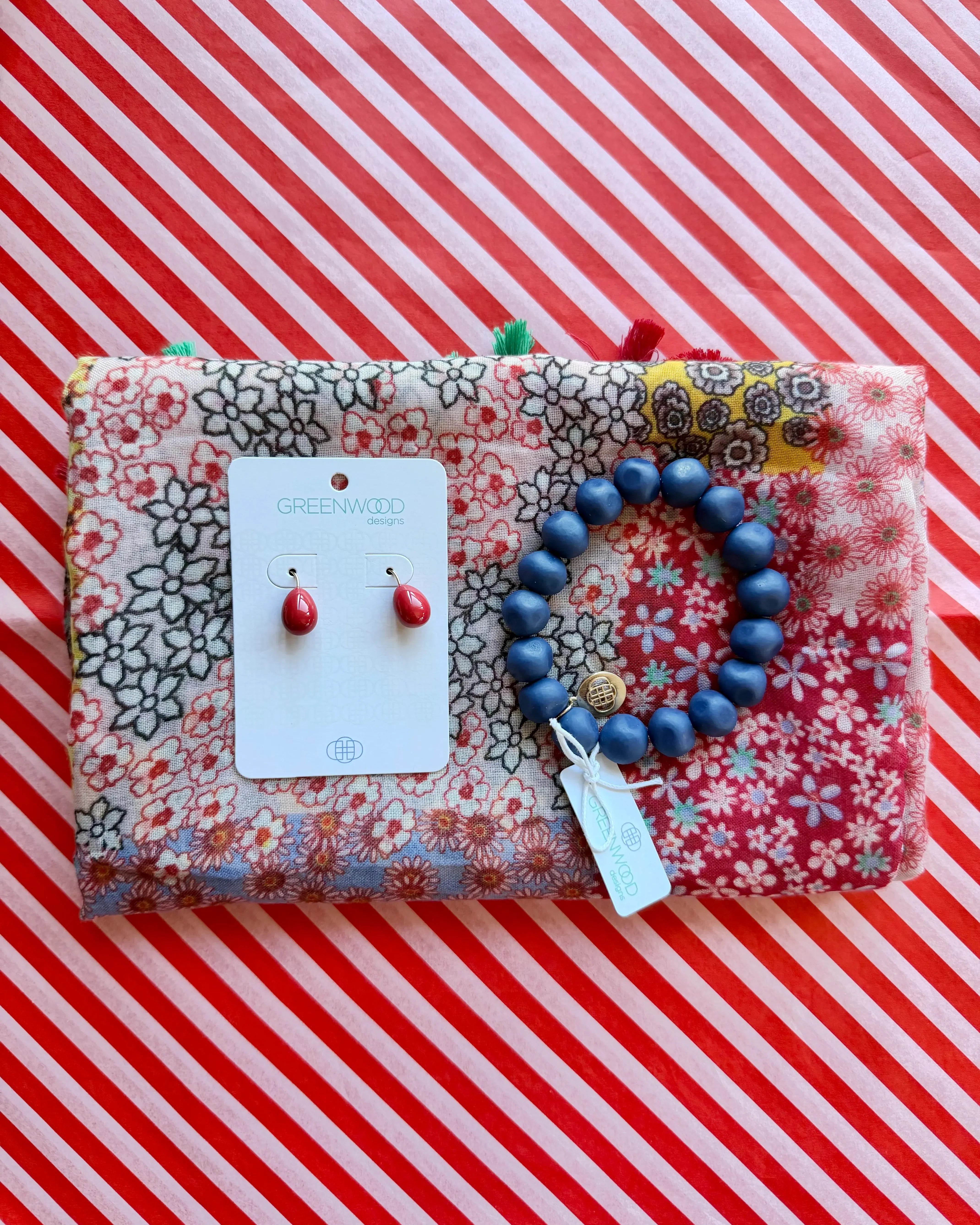 Flat lay of the Willow scarf in Red, a red, pink and black patchwork floral print, the Blue rock bracelet and Alice earrings in Red on a Greenwood Designs card.