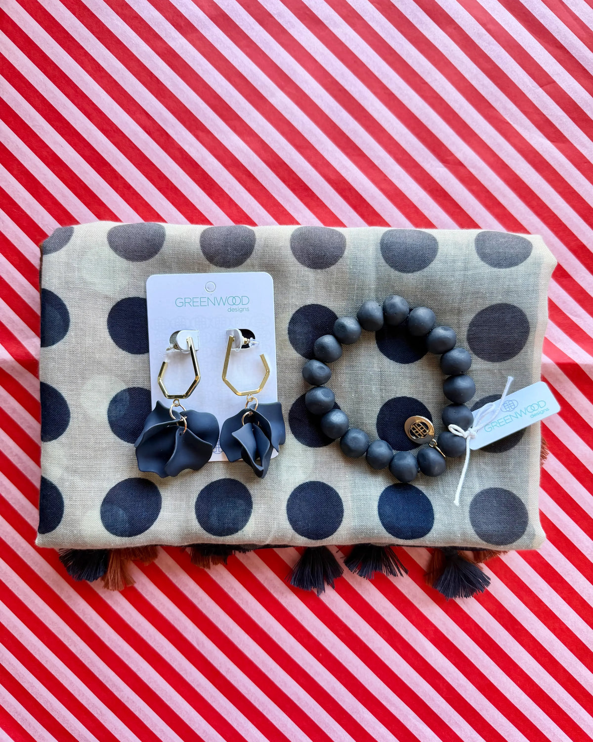 Flat lay of the Nina scarf in taupe with navy polka dots and tassels, the Navy rock bracelet and Petunia earrings in Navy on a Greenwood Designs card.