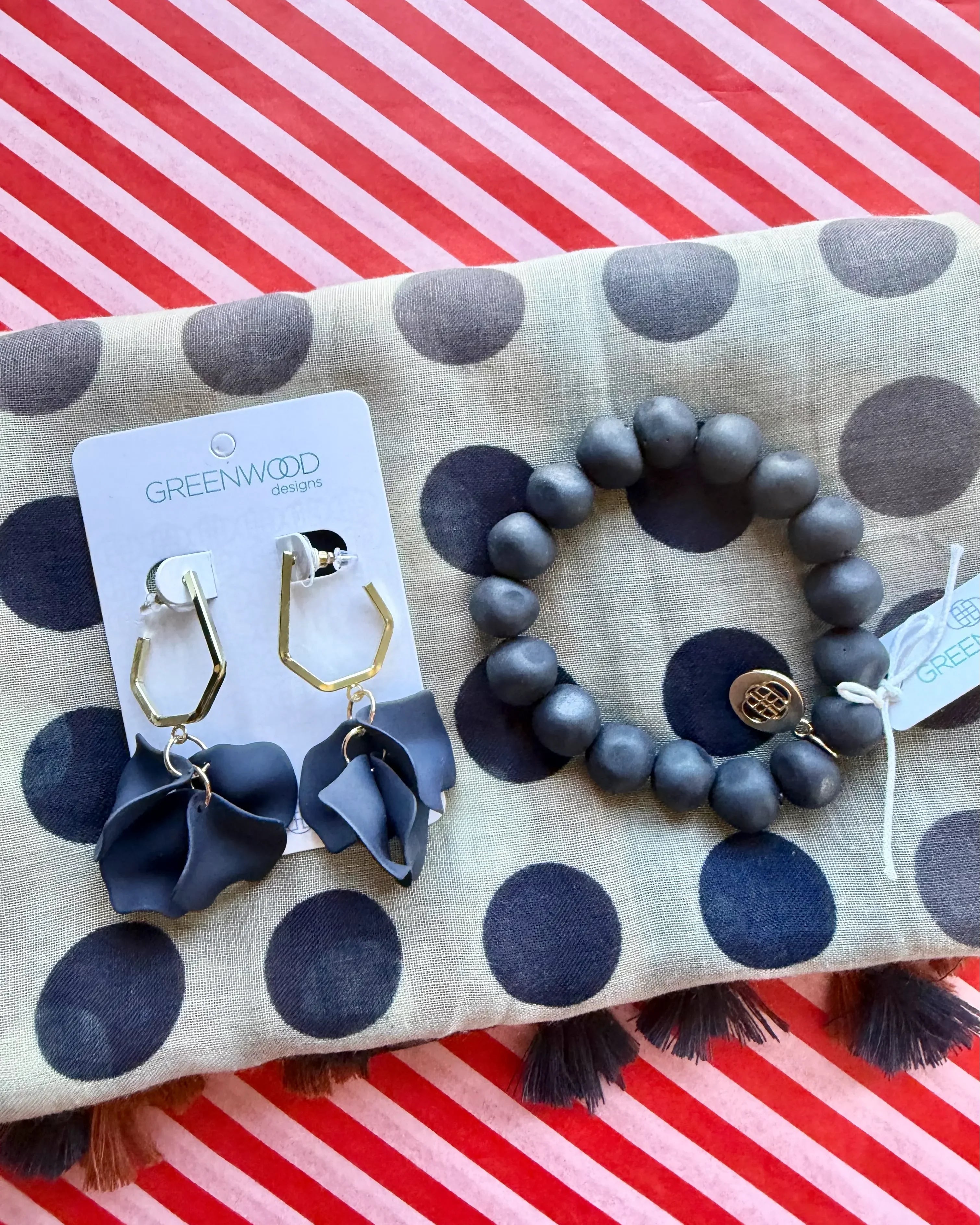 Close-up of the Nina scarf in taupe with navy polka dots, the Navy rock bracelet and Petunia earrings in Navy, gold hexagon drops with navy petals, on a Greenwood Designs card.