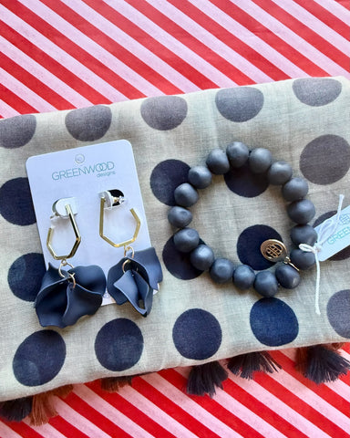 Close-up of the Nina scarf in taupe with navy polka dots, the Navy rock bracelet and Petunia earrings in Navy, gold hexagon drops with navy petals, on a Greenwood Designs card.