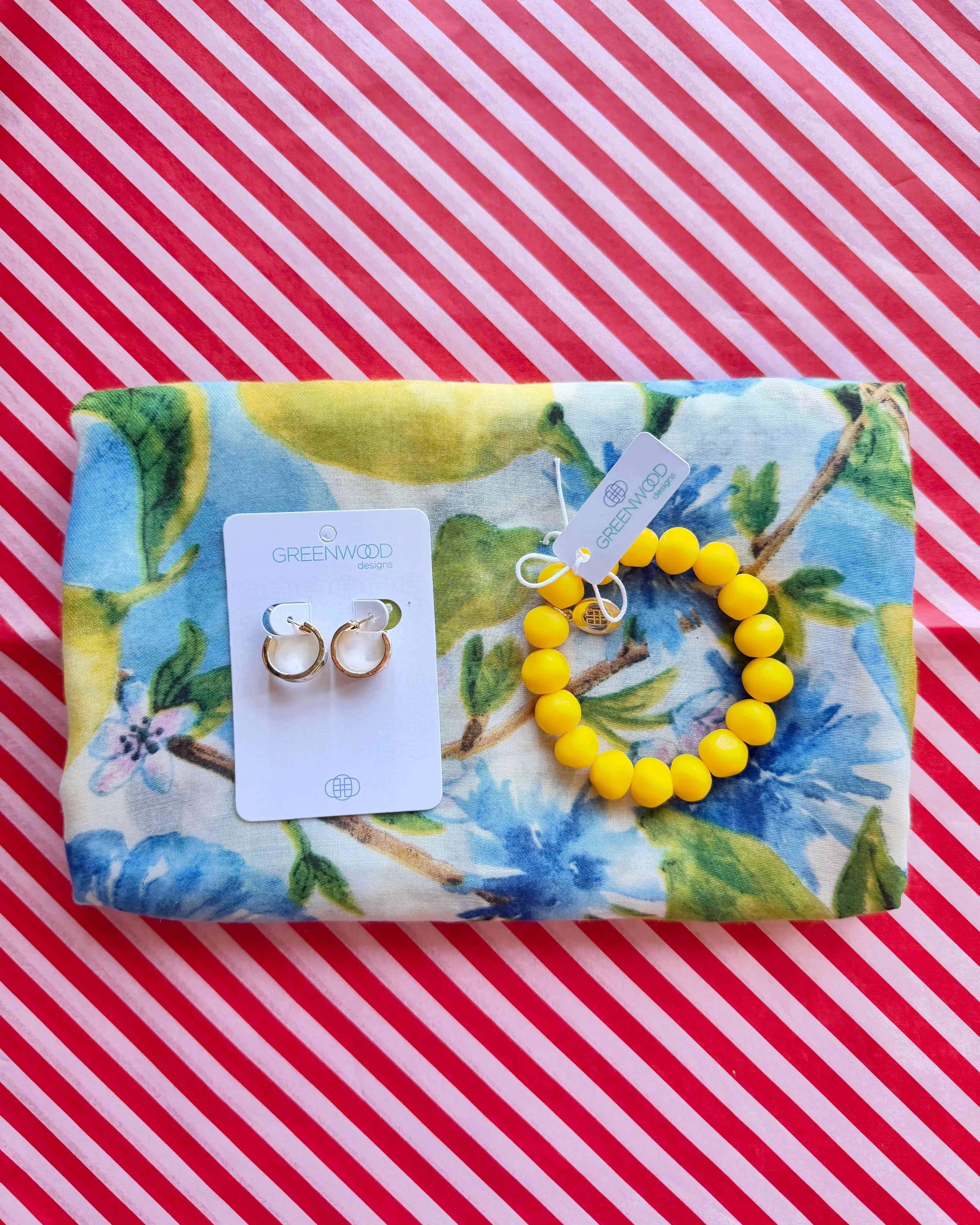 Flat lay of the Iris scarf in a lemon and blue watercolour floral print, the Yellow rock bracelet and Hayley earrings, gold and white enamel huggie hoops, on a Greenwood Designs card.