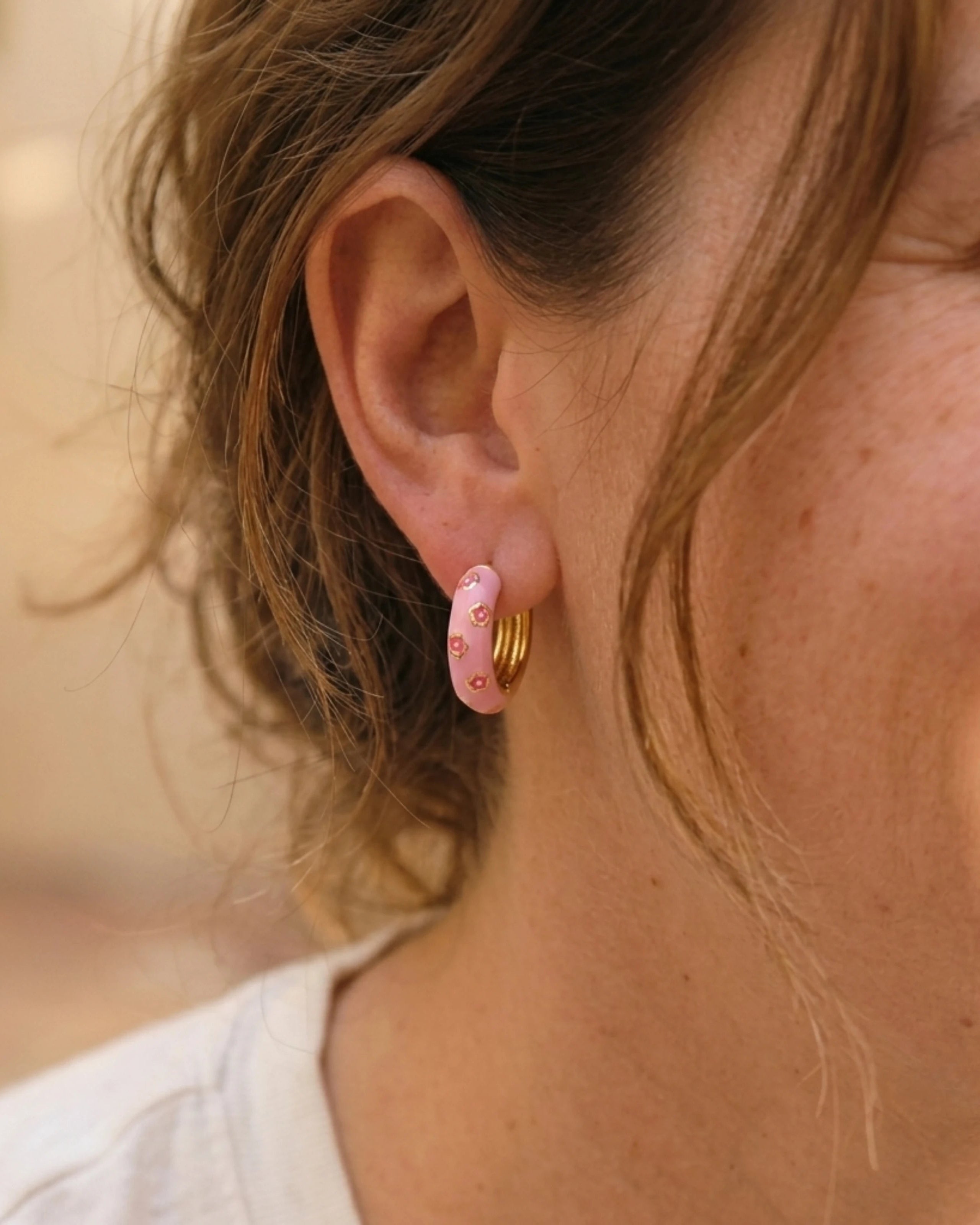 Woman wearing light pink enamel gold hoop earrings with pink flower pattern