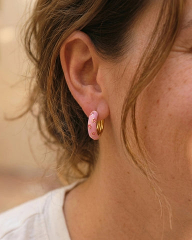 Woman wearing light pink enamel gold hoop earrings with pink flower pattern