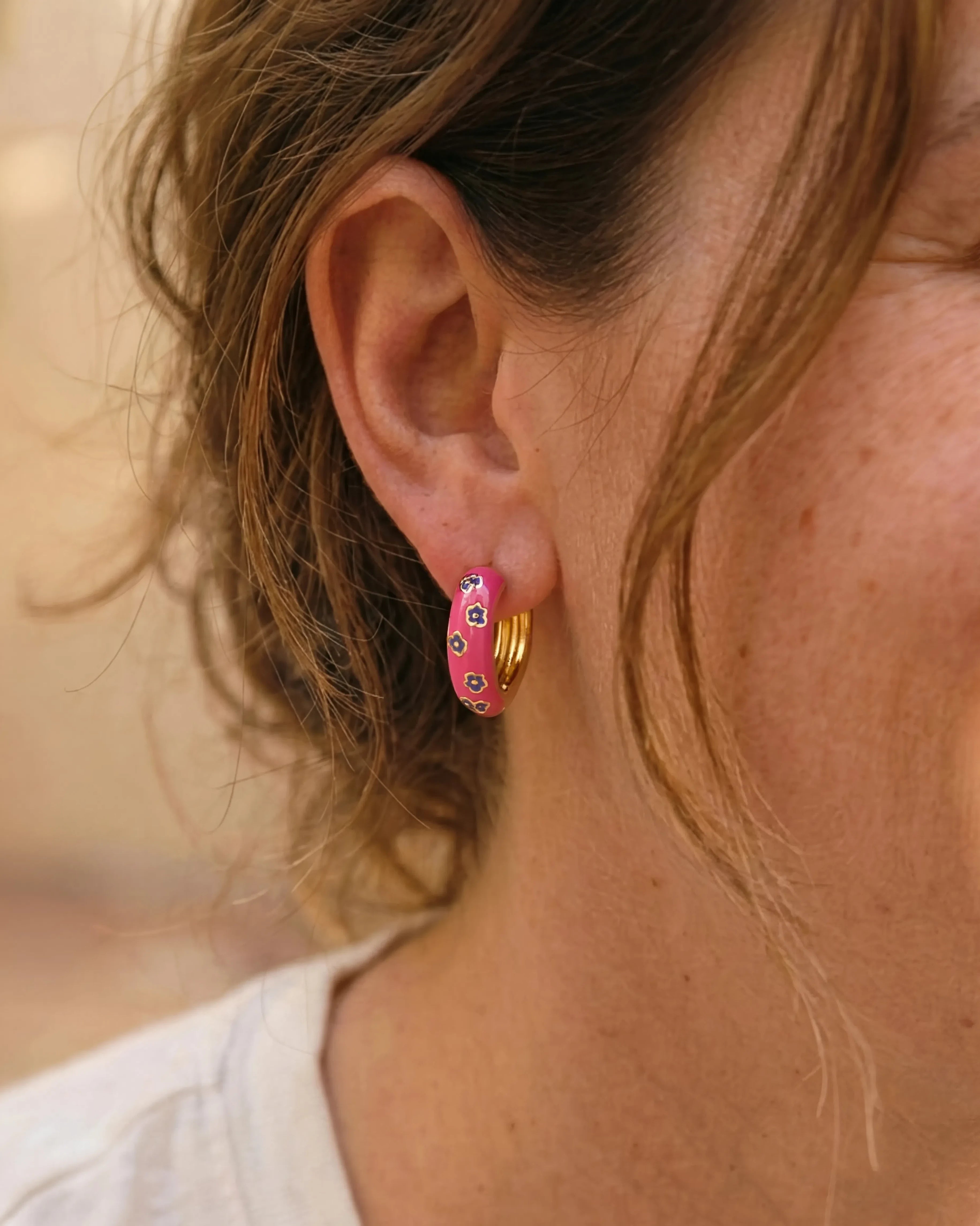 Woman wearing pink enamel gold hoop earrings with purple flower pattern