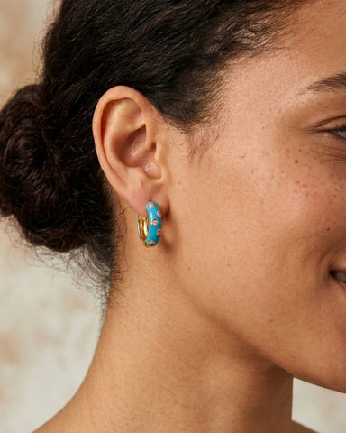 Woman wearing blue enamel gold hoop earrings with pink flower pattern
