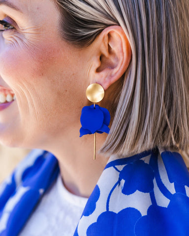Close-up of a woman wearing blue floral earrings with a gold accent.