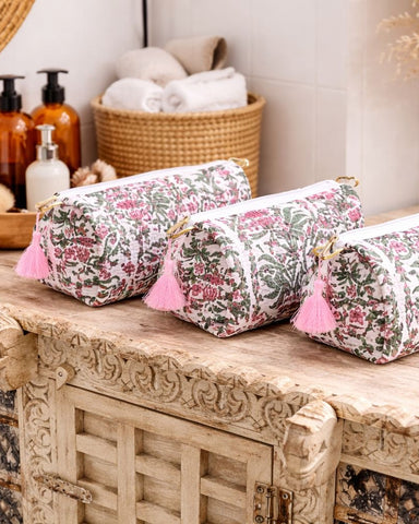 Three floral-patterned cosmetic bags with pink tassels on a wooden surface.