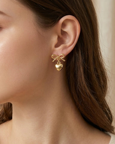 Woman wearing gold bow earrings with heart dangle detail