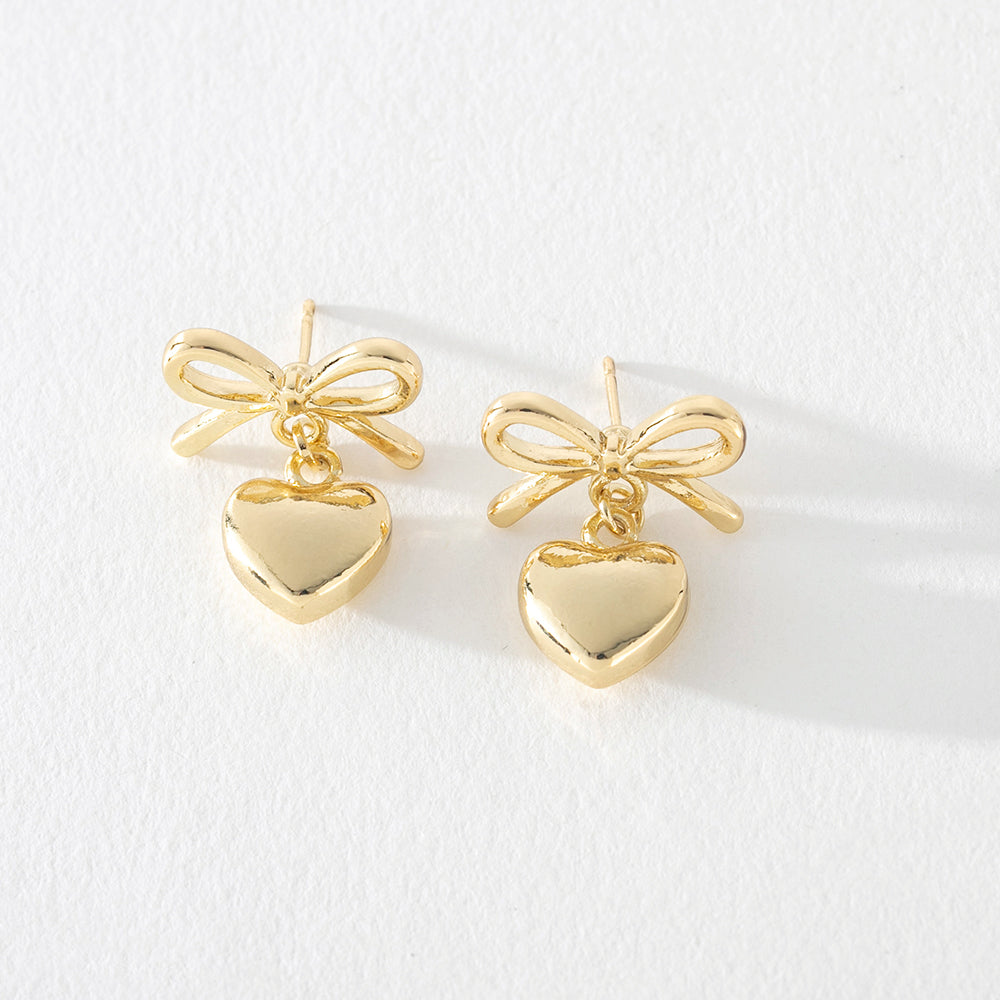 Gold bow earrings with heart dangle detail on white background