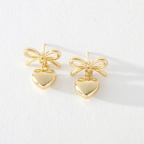 Gold bow earrings with heart dangle detail on white background