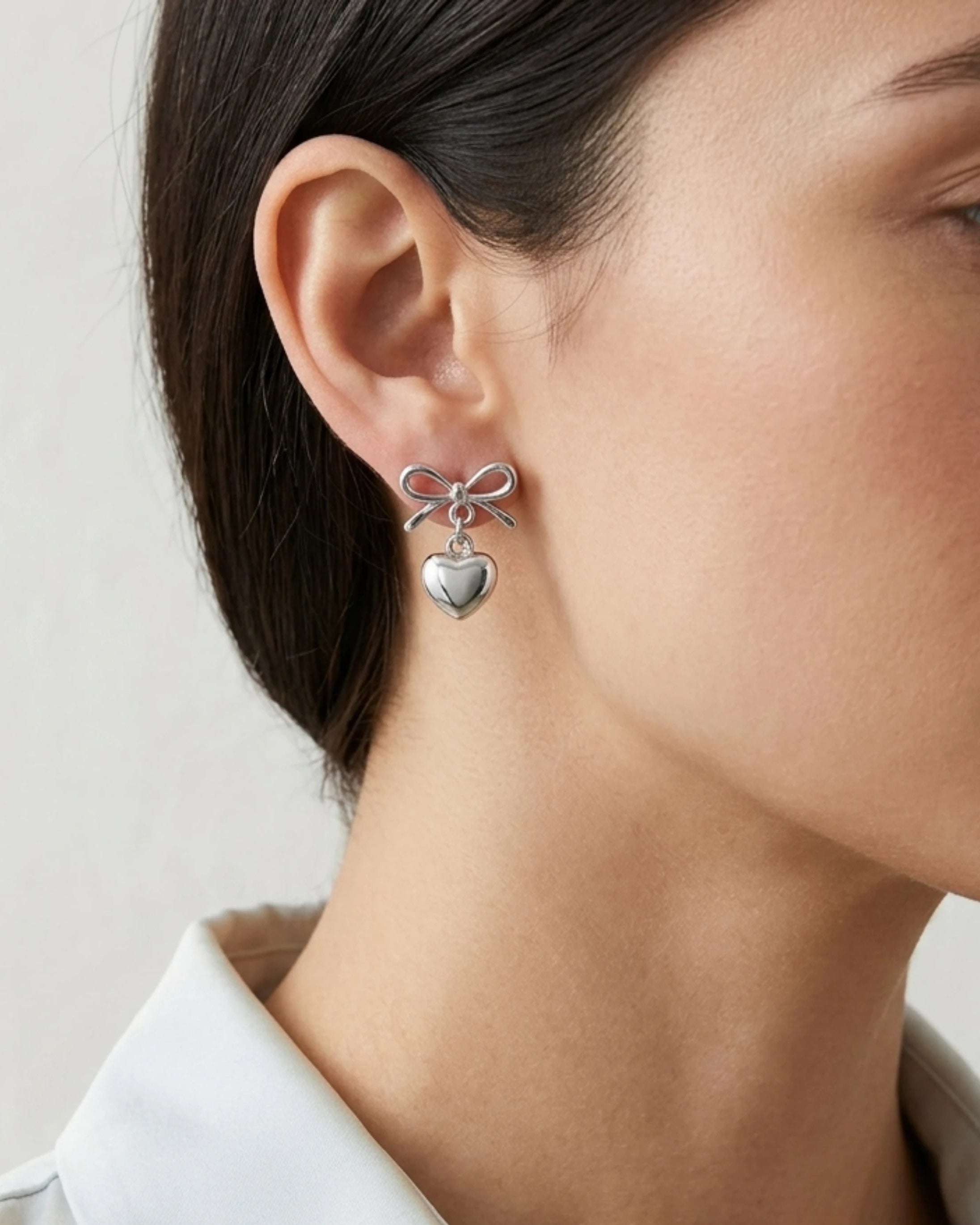 Woman wearing silver bow earrings with heart dangle detail