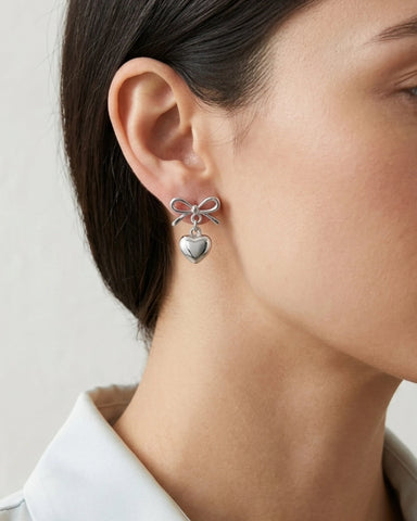 Woman wearing silver bow earrings with heart dangle detail