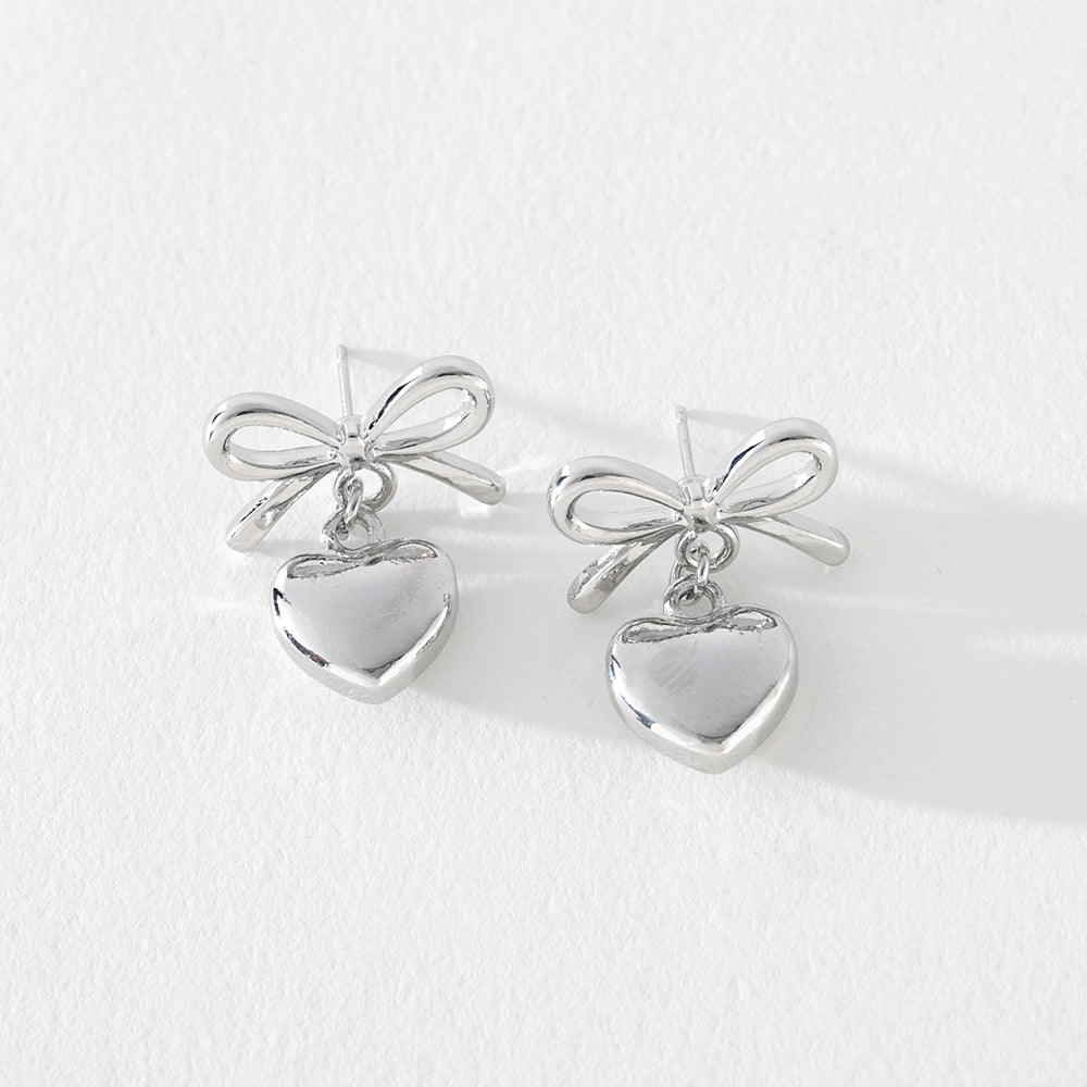 Silver bow earrings with heart dangle detail on white background