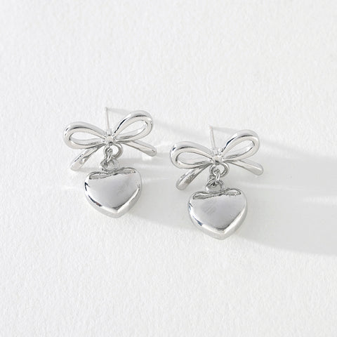 Silver bow earrings with heart dangle detail on white background