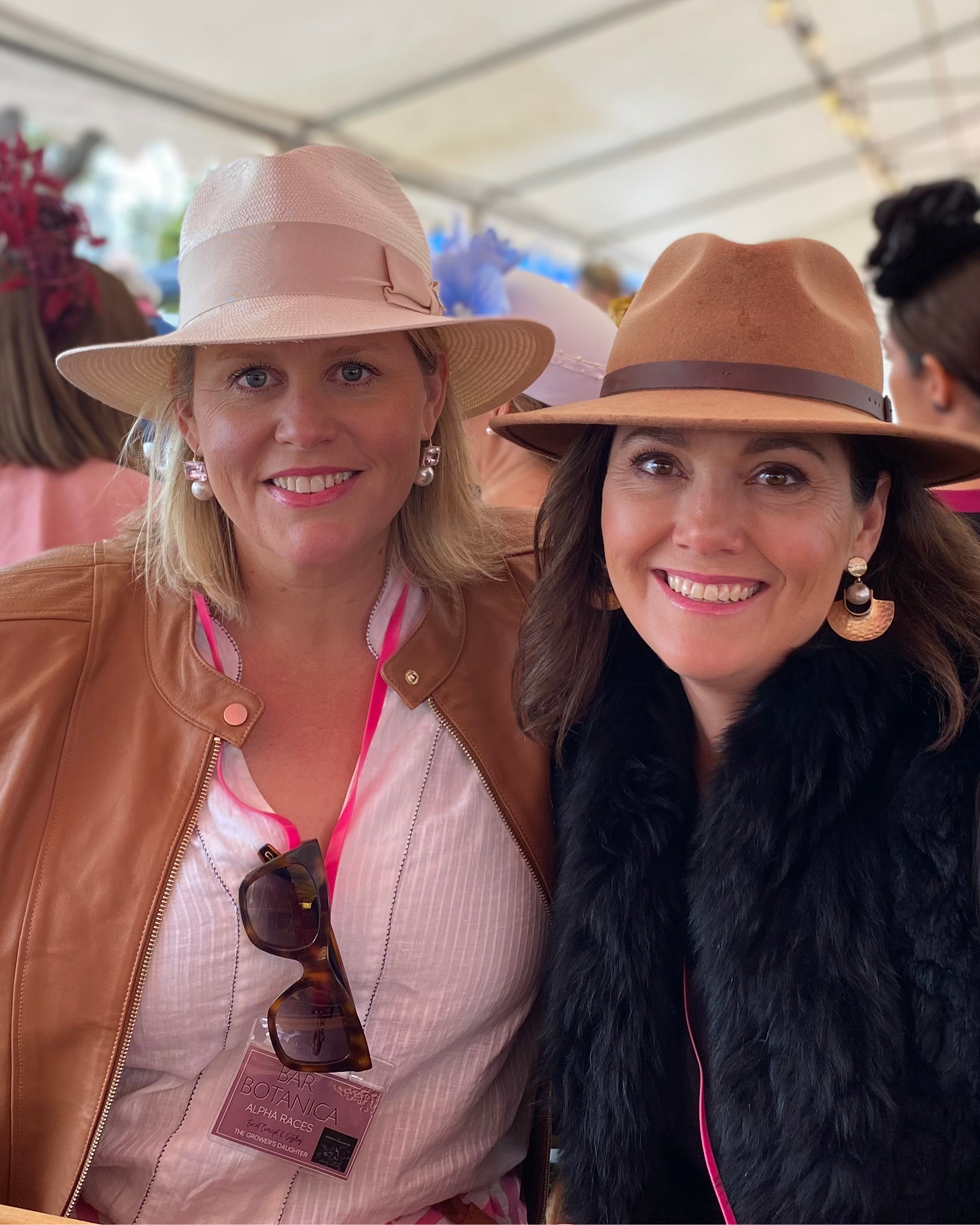 Two women wearing hats and smiling at a social event.
