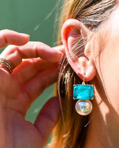 Close-up of a person wearing a turquoise earring with a pearl drop.