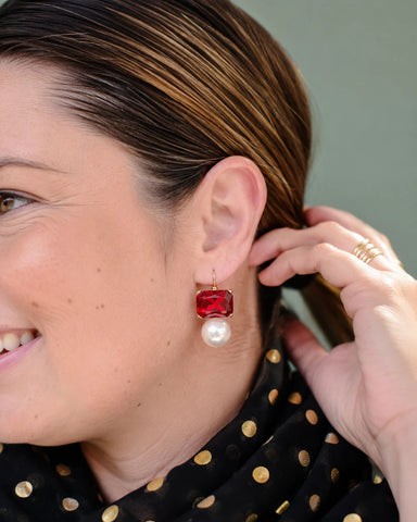 Close-up of a woman wearing a red and pearl earring with a blurred background